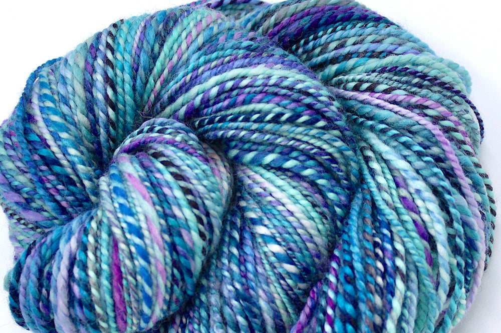 A close up view of a one of a kind, Dk Weight, hand dyed variegated skein of multicolored Blue, Pink, and Purple self-striping Hand spun Yarn, made of 100% Hand Dyed Superwash Merino Wool. 