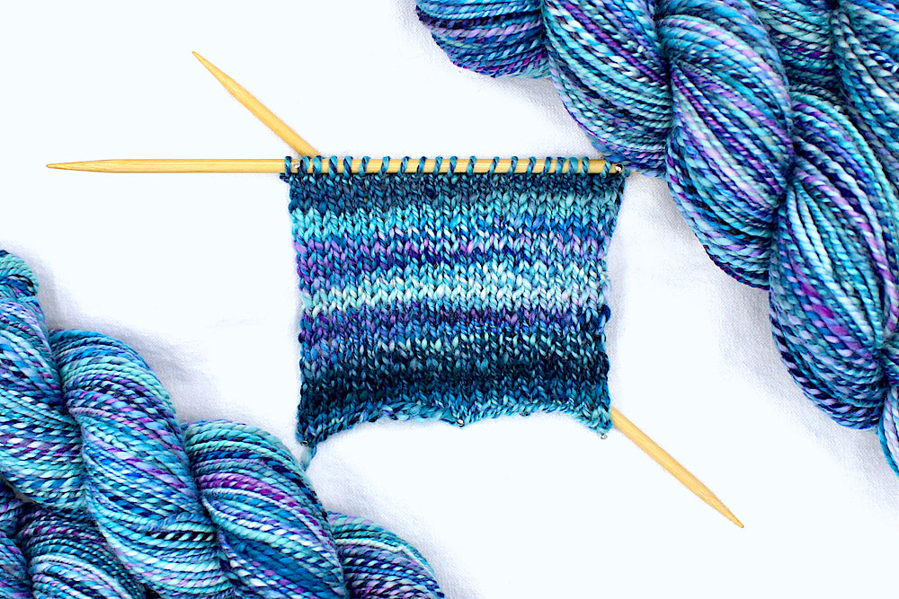 A sample swatch knitted on size 5 knitting needles from a one of a kind, Dk Weight, hand dyed variegated skein of multicolored Blue, Pink, and Purple self-striping Hand spun Yarn, made of 100% Hand Dyed Superwash Merino Wool. 