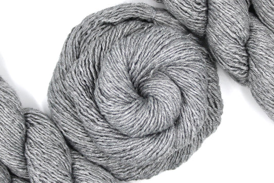 A skein of Silver Grey, Acrylic/ Nylon/ Wool, Sport weight Yarn recycled by hand from unwanted sweaters swirled attractively in the center of the frame. 