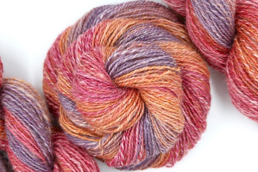 A one of a kind, hand dyed gradient skein of multicolored pastel Red, Orange, Light Peach, and Purple self-striping wool Yarn coiled attractively in the center of the frame. 