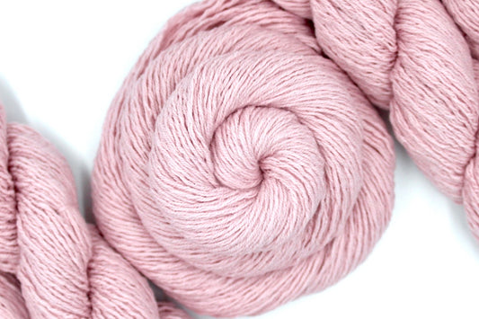 A skein of Vegan, Light Ballet Pink, Cotton/ Acrylic, Sport weight Yarn recycled by hand from unwanted sweaters swirled attractively in the center of the frame. 