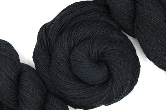 A skein of Vegan, Black, 100% Cotton, Fingering weight Yarn recycled by hand from unwanted sweaters swirled attractively in the center of the frame. 