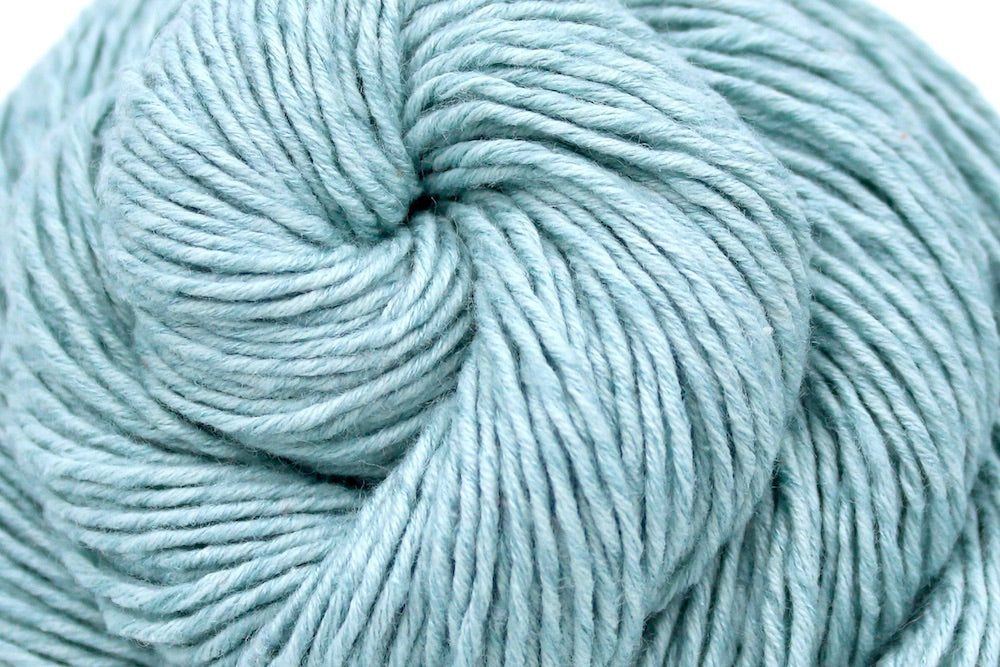 A close up shot of a skein of Vegan, Pastel Baby Blue, Cotton/ Acrylic, Dk weight Yarn recycled by hand from unwanted sweaters beautifully coiled in the center of the frame. 