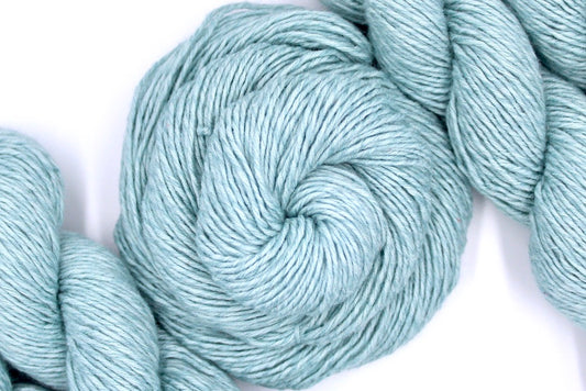 A skein of Vegan, Pastel Baby Blue, Cotton/ Acrylic, Dk weight Yarn recycled by hand from unwanted sweaters swirled attractively in the center of the frame. 