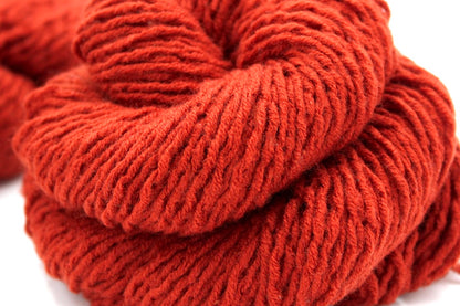 A close up shot of a skein of Vegan, Rusty Orange, 100% Acrylic, Worsted weight Yarn recycled by hand from unwanted sweaters beautifully coiled in the center of the frame. 