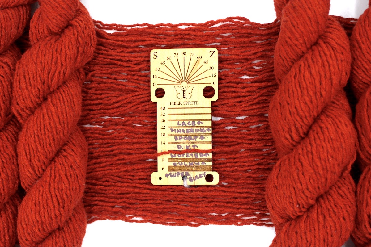 A skein of Vegan, Rusty Orange, 100% Acrylic, Worsted Weight Yarn recycled by hand from unwanted sweaters draped over a Llama shaped Yarn weight tool. 