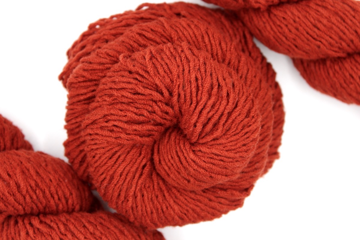 A skein of Vegan, Rusty Orange, 100% Acrylic, Worsted weight Yarn recycled by hand from unwanted sweaters swirled attractively in the center of the frame. 