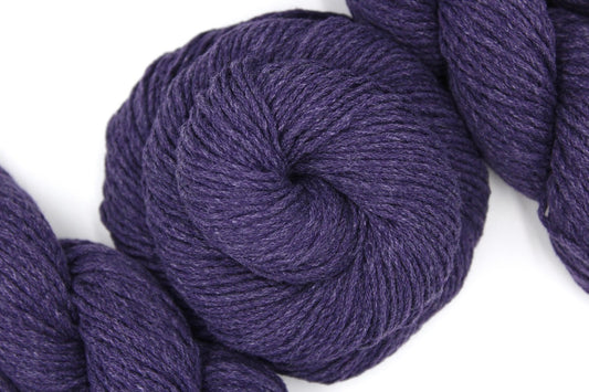 A skein of Vegan, Dark Purple, Cotton/ Acrylic, Worsted weight Yarn recycled by hand from unwanted sweaters swirled attractively in the center of the frame. 