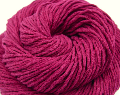 A close up shot of a skein of Vegan, Raspberry Red, 100% Cotton, Worsted weight Yarn recycled by hand from unwanted sweaters beautifully coiled in the center of the frame. 