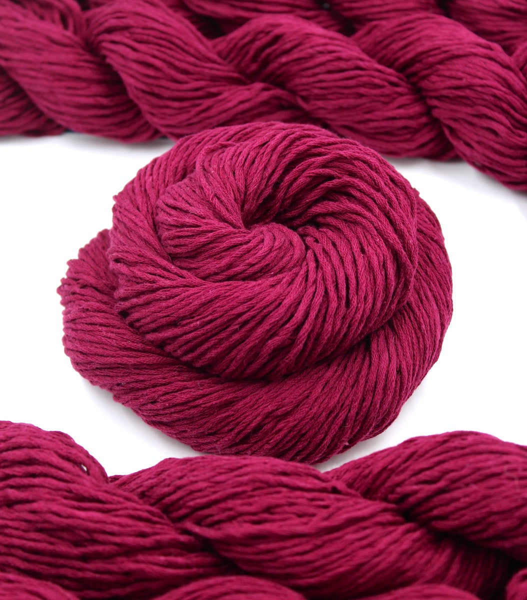 A skein of Vegan, Raspberry Red, 100% Cotton, Worsted weight Yarn recycled by hand from unwanted sweaters swirled attractively in the center of the frame. 