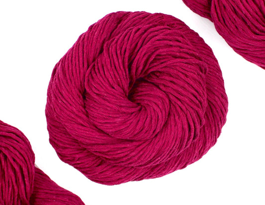 A skein of Vegan, Raspberry Red, 100% Cotton, Worsted weight Yarn recycled by hand from unwanted sweaters swirled attractively in the center of the frame. 