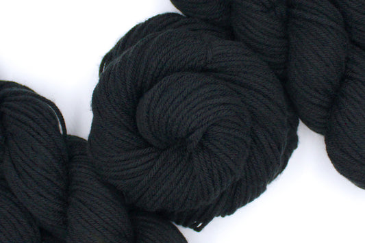 A skein of Vegan, Black, 100% Acrylic, Worsted weight Yarn recycled by hand from unwanted sweaters swirled attractively in the center of the frame. 