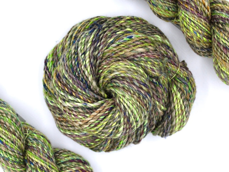 A one of a kind, hand dyed Variegated skein of multicolored Lime Green, Yellow, Maroon and Navy Blue self-striping wool Yarn coiled attractively in the center of the frame. 