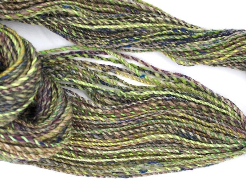 A one of a kind, hand dyed Variegated skein of multicolored Lime Green, Yellow, Maroon and Navy Blue self-striping wool Yarn draped diagonally across the frame, so you can really see the color play. 
