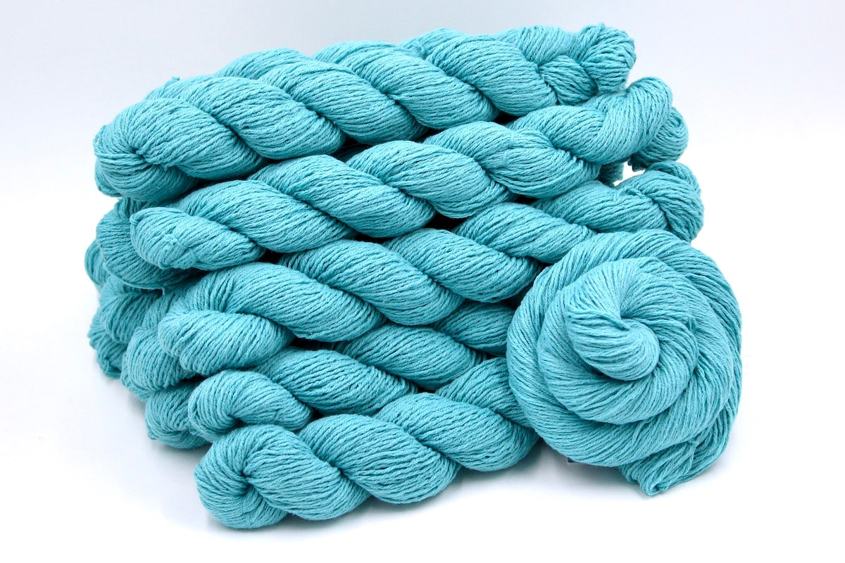 A close up shot of a skein of Vegan, Robin’s Egg Blue, Cotton/ Acrylic, Sport weight Yarn recycled by hand from unwanted sweaters beautifully coiled in the center of the frame. 