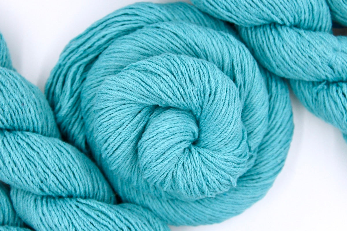 A skein of Vegan, Robin’s Egg Blue, Cotton/ Acrylic, Sport weight Yarn recycled by hand from unwanted sweaters swirled attractively in the center of the frame.