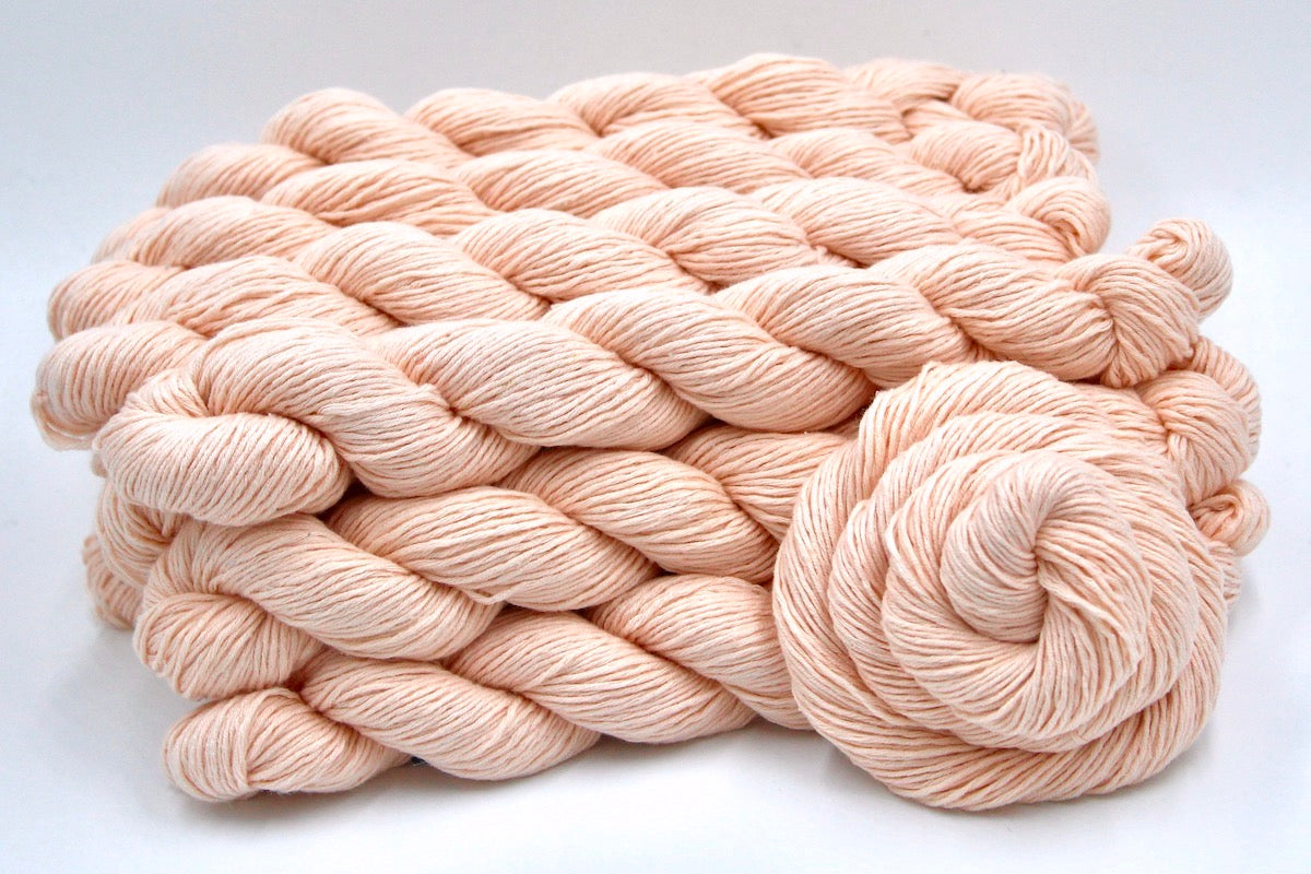 Several skeins of Vegan, Light Pastel Peach/ Pink, Cotton/ Rayon/ Nylon, Sport weight recycled by hand from unwanted sweaters stacked on top of each other attractively. 