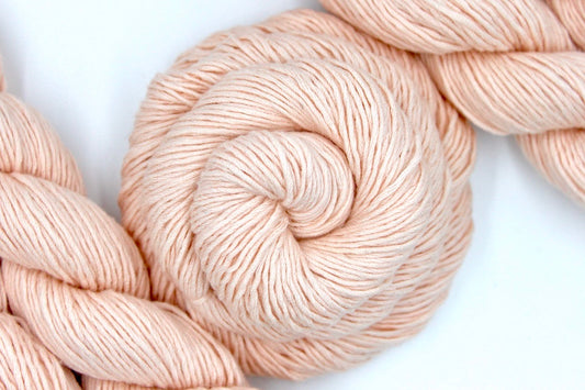 A skein of Vegan, Light Pastel Peach/ Pink, Cotton/ Rayon/ Nylon, Sport weight Yarn recycled by hand from unwanted sweaters swirled attractively in the center of the frame.