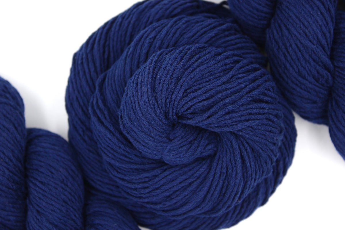 A skein of Vegan, Sailor Navy Blue, Cotton/ Polyester/ Acrylic, Dk weight Yarn recycled by hand from unwanted sweaters swirled attractively in the center of the frame. 