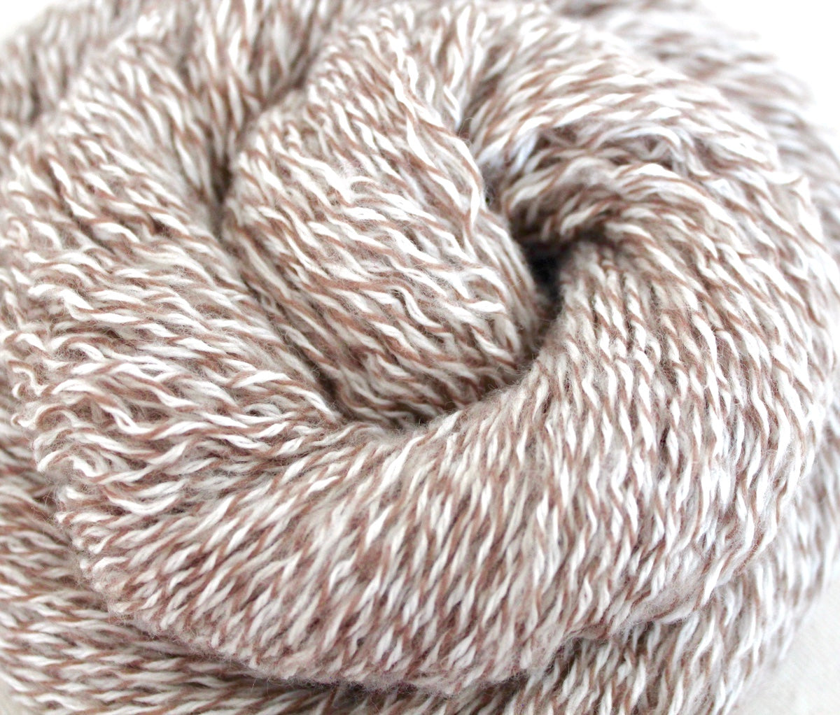 A close up shot of a skein of Vegan, Variegated Tan and White, 100% Acrylic, Sport weight Yarn recycled by hand from unwanted sweaters beautifully coiled in the center of the frame. 