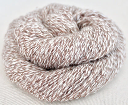 A skein of Vegan, Variegated Tan and White, 100% Acrylic, Sport weight Yarn recycled by hand from unwanted sweaters swirled attractively in the center of the frame. 