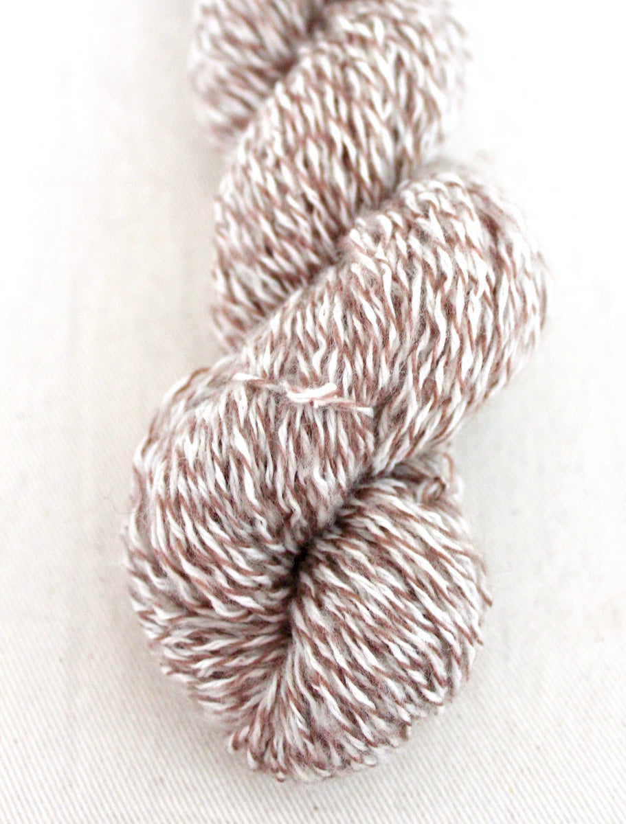 A close up shot of a skein of Vegan, Variegated Tan and White, 100% Acrylic, Sport weight Yarn recycled by hand from unwanted sweaters beautifully coiled in the center of the frame. 