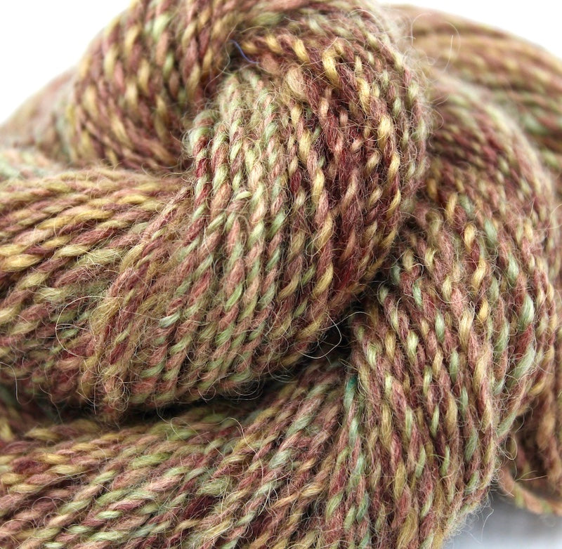 A close up view of a one of a kind, hand dyed variegated skein of multicolored Reddish Brown, Green, Taupe, and Gold self-striping wool Yarn. 