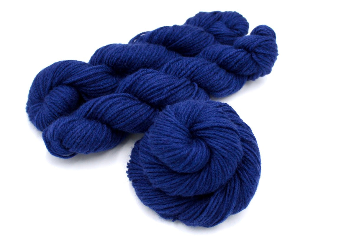 Several skeins of Vegan, Navy Sapphire Blue, 100% Acrylic, Worsted weight recycled by hand from unwanted sweaters stacked on top of each other attractively. 