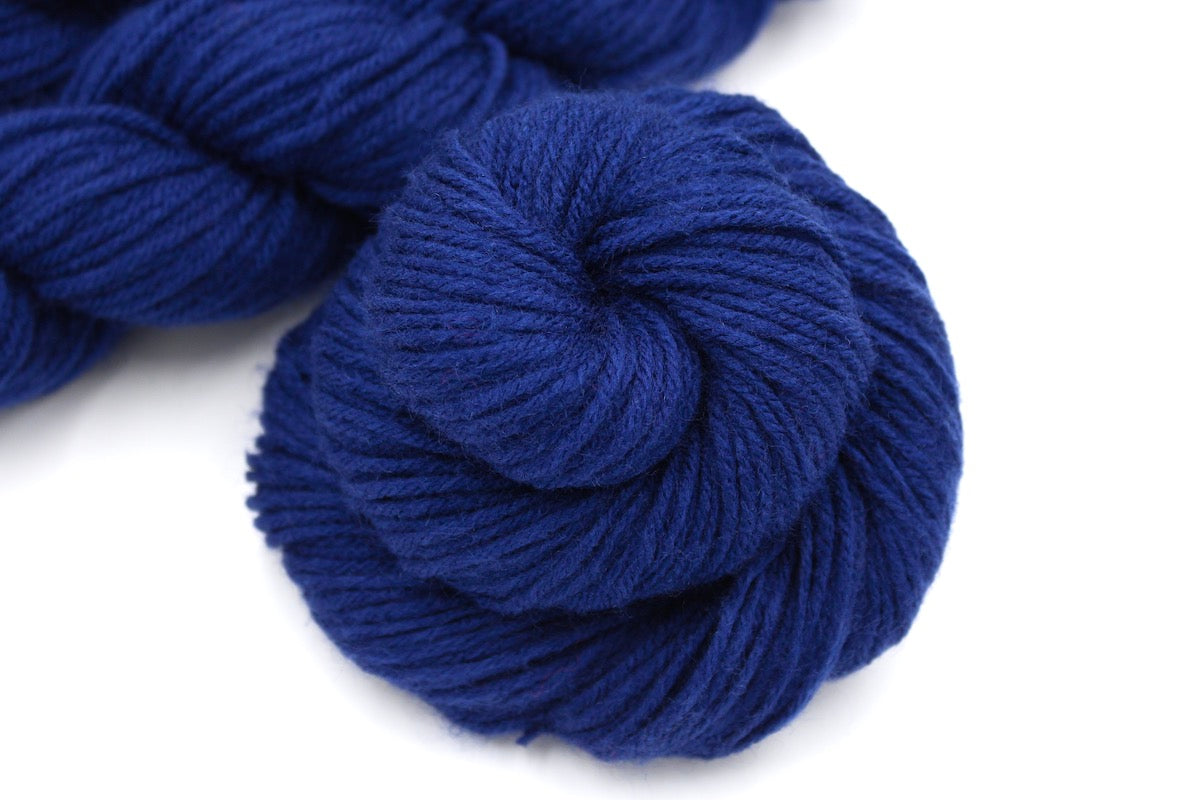 A close up shot of a skein of Vegan, Navy Sapphire Blue, 100% Acrylic, Worsted weight Yarn recycled by hand from unwanted sweaters beautifully coiled in the center of the frame. 