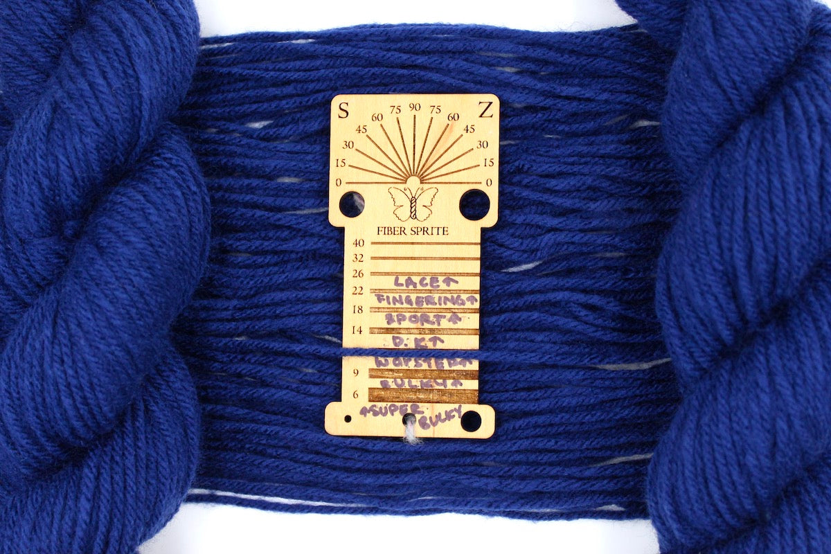 A skein of Vegan, Navy Sapphire Blue, 100% Acrylic, Worsted Weight Yarn recycled by hand from unwanted sweaters draped over a Llama shaped Yarn weight tool. 