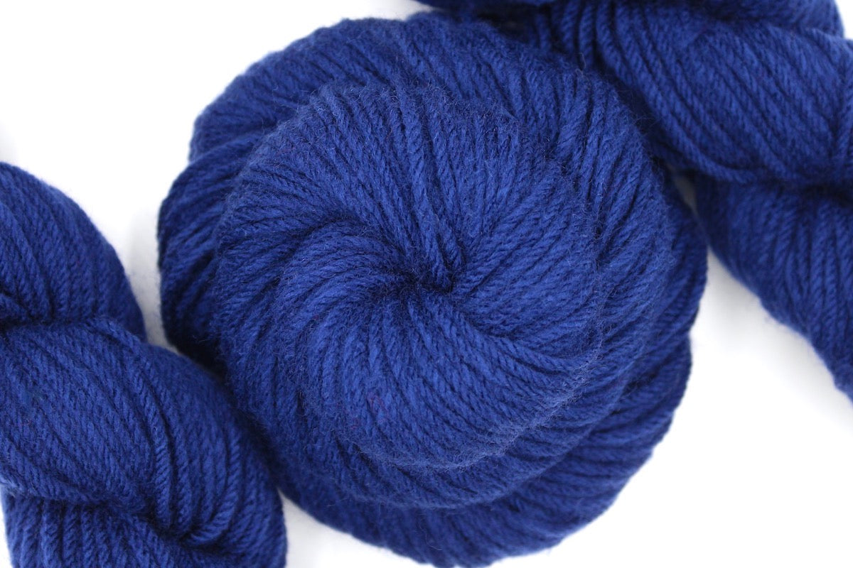 A skein of Vegan, Navy Sapphire Blue, 100% Acrylic, Worsted weight Yarn recycled by hand from unwanted sweaters swirled attractively in the center of the frame. 