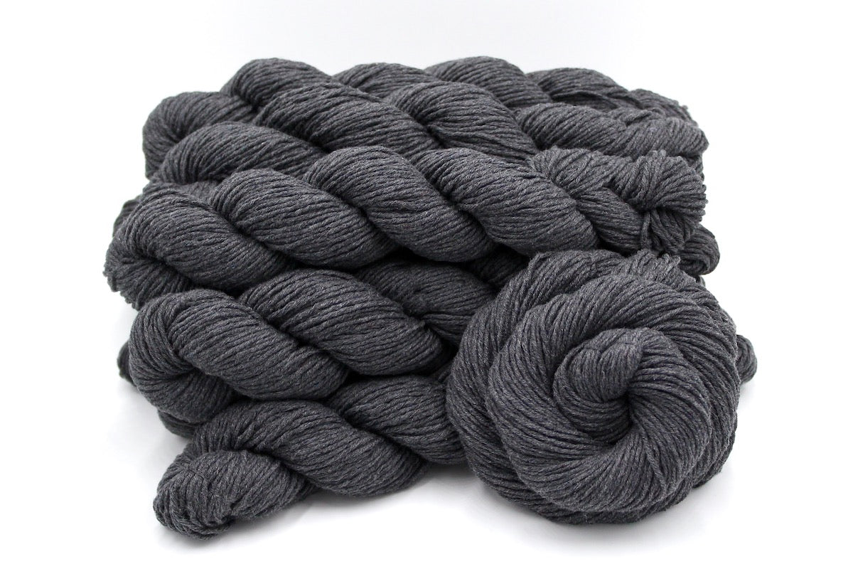 Several skeins of Vegan, Dark Heathered Charcoal Grey, 100% Cotton, Worsted weight recycled by hand from unwanted sweaters stacked on top of each other attractively. 