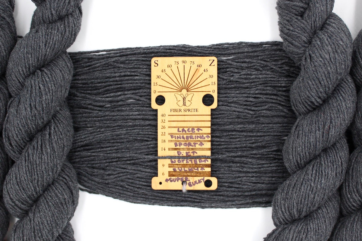 A skein of Vegan, Dark Heathered Charcoal Grey, 100% Cotton, Worsted Weight Yarn recycled by hand from unwanted sweaters draped over a Llama shaped Yarn weight tool. 