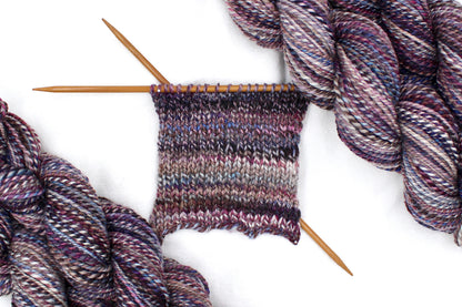 A sample swatch knitted on size 5 knitting needles from a one of a kind, Dk Weight, hand dyed variegated skein of multicolored Maroon, Burgandy, Purple, Grey, and Blue self-striping 100% Superwash Merino wool Yarn. 