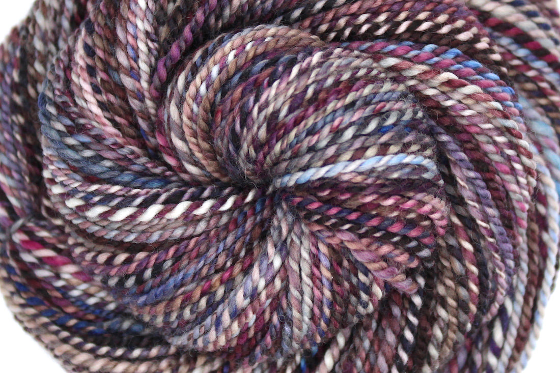 A close up view of a one of a kind, Dk Weight, hand dyed variegated skein of multicolored Maroon, Burgandy, Purple, Grey, and Blue self-striping 100% Superwash Merino wool Yarn. 