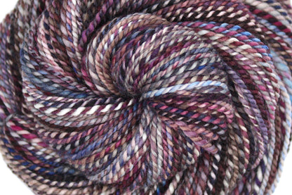 A close up view of a one of a kind, Dk Weight, hand dyed variegated skein of multicolored Maroon, Burgandy, Purple, Grey, and Blue self-striping 100% Superwash Merino wool Yarn. 