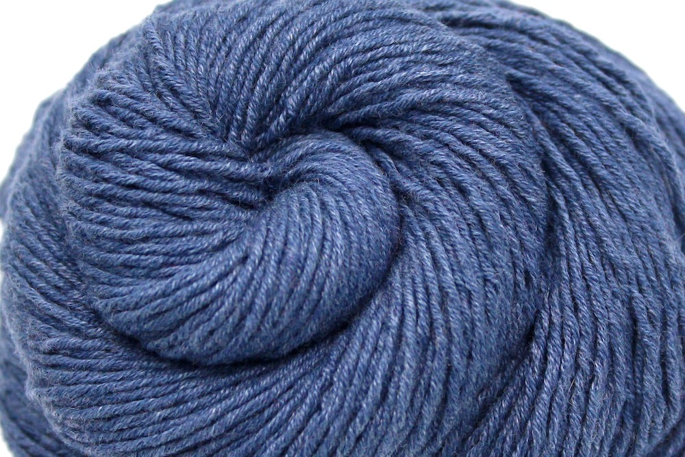 A close up shot of a skein of Vegan, Heathered Slate Grayish Blue, Cotton/ Acrylic, Sport weight Yarn recycled by hand from unwanted sweaters beautifully coiled in the center of the frame. 