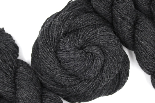 A skein of Heathered Dark Charcoal Grey, 100% Merino Wool, Dk weight Yarn recycled by hand from unwanted sweaters swirled attractively in the center of the frame. 