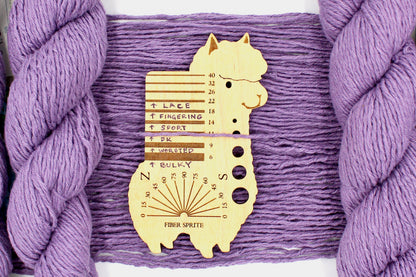A skein of Vegan, Dusky Lavender, 60% Cotton, 40% Acrylic, DK Weight Yarn recycled by hand from unwanted sweaters draped over the center of the frame with one strand on top of a Llama shaped Yarn weight tool, to better illustrate the thickness of the yarn. 