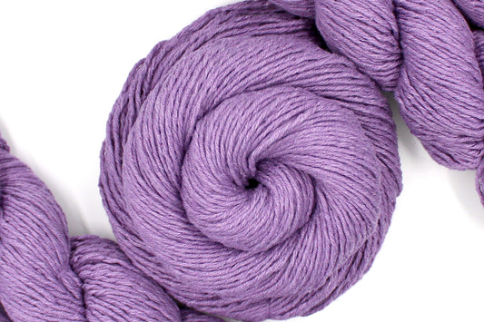 A skein of Vegan, Dusky Lavender, 60% Cotton, 40% Acrylic, DK weight Yarn recycled by hand from unwanted sweaters swirled attractively in the center of the frame. 