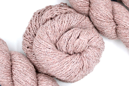 A skein of Vegan, Dusky Pink, Cotton, Polyester, Acrylic, Nylon, Sport Weight Yarn recycled by hand from unwanted sweaters swirled attractively in the center of the frame. 