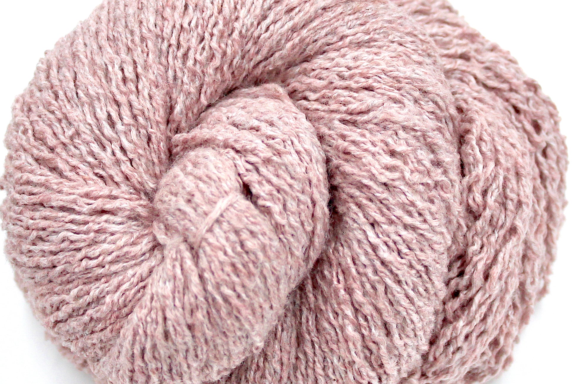 A close up shot of a skein of Vegan, Dusky Pink, Cotton, Polyester, Acrylic, Nylon, Sport Weight Yarn recycled by hand from unwanted sweaters beautifully coiled in the center of the frame. 