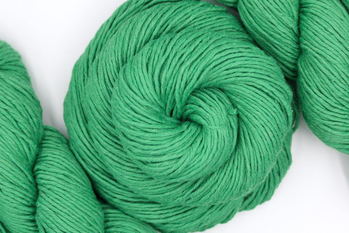 A skein of Vegan, Bright Spearmint Green, 100% Cotton, Worsted weight Yarn recycled by hand from unwanted sweaters swirled attractively in the center of the frame. 