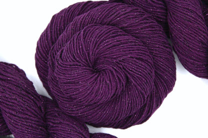 A skein of Vegan, Deep Plum Purple, Cotton/ Polyester/ Sparkle Fiber, Sport weight Yarn recycled by hand from unwanted sweaters swirled attractively in the center of the frame. 