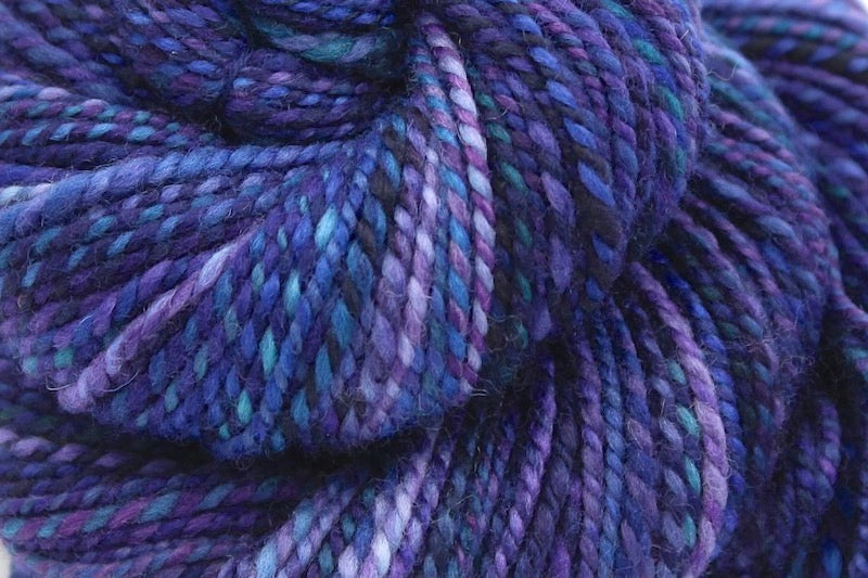 A close up view of a one of a kind, hand dyed variegated skein of multicolored Navy Blue, Plum, Sapphire Blue, Teal and Lavender self-striping wool Yarn. 
