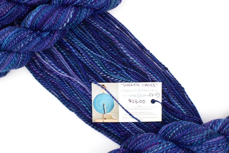 A one of a kind, hand dyed variegated skein of multicolored Navy Blue, Plum, Sapphire Blue, Teal and Lavender self-striping wool Yarn draped diagonally across the frame, so you can really see the color play. 