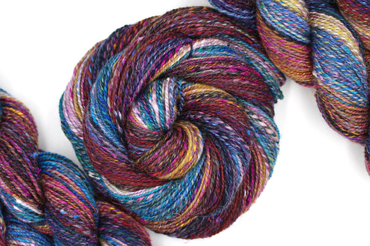 A one of a kind, hand dyed gradient skein of multicolored Navy Blue, Dark Red, Fuchsia, Orange, Yellow, Pink, and Sky Blue self-striping wool Yarn coiled attractively in the center of the frame. 