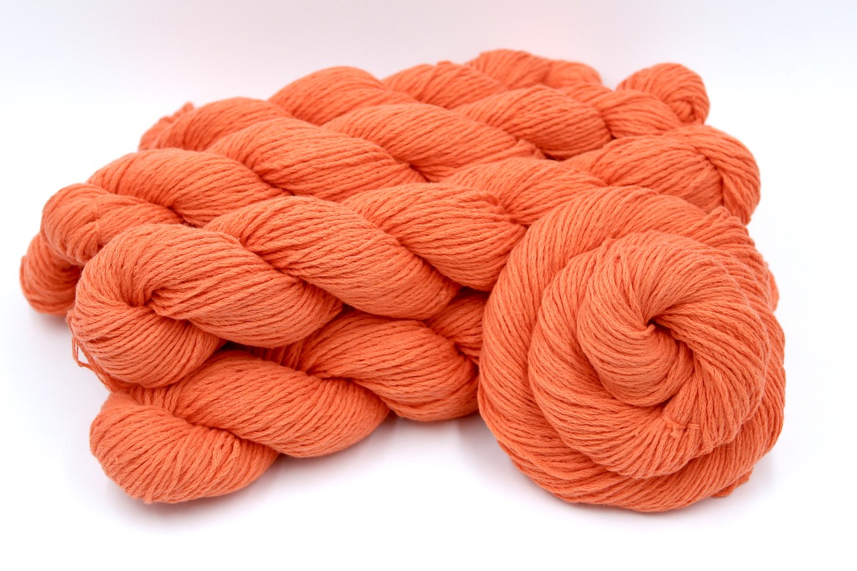 Several skeins of Vegan, Neon Tangerine Orange, Cotton/ Nylon, Dk weight recycled by hand from unwanted sweaters stacked on top of each other attractively. 