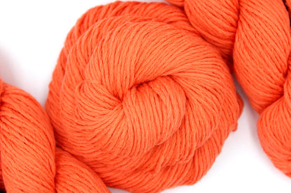 A skein of Vegan, Neon Tangerine Orange, Cotton/ Nylon, Dk weight Yarn recycled by hand from unwanted sweaters swirled attractively in the center of the frame. 