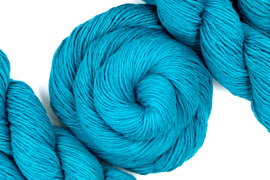 A skein of Vegan, Teal blue, 100% Cotton, Sport Weight Yarn recycled by hand from unwanted sweaters swirled attractively in the center of the frame. 